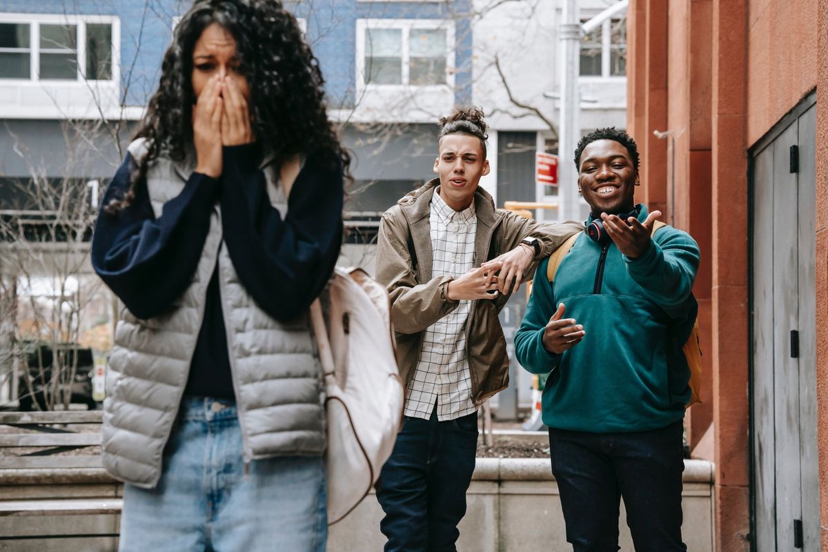 Young woman covering her face, visibly upset, while two young men look on in the street